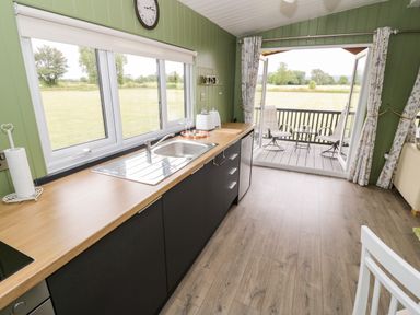 A kitchen area with a wooden countertop, sink, and cabinets looking out to a patio with chairs at Cotswold View 1 in Honeybourne