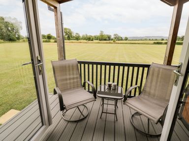 A porch with two chairs and a table with two mugs overlooking a field at Cotswold View 1 in Honeybourne