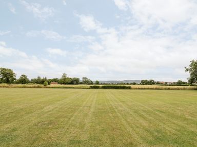 A large grassy field with trees and a few buildings in the distance at Cotswold View 1 in Honeybourne