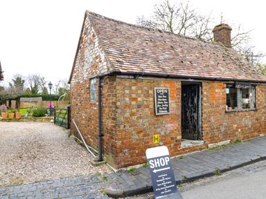 A brick building with a shop sign and a gravel driveway at Cotswold View 1 in Honeybourne