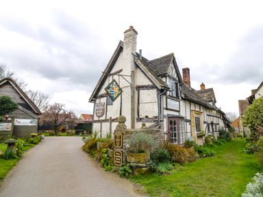 An old pub building with timber framing and gardens alongside a paved road at Cotswold View 1 in Honeybourne
