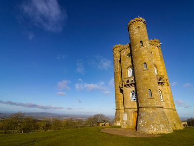 A stone tower on a grassy hill with trees and a blue sky at Cotswold View 1 in Honeybourne
