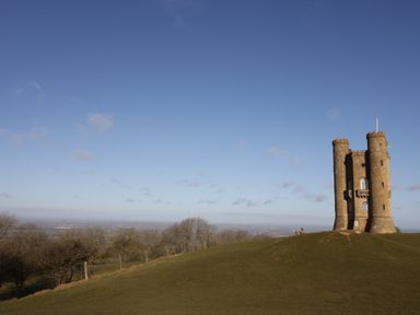 A stone tower on a grassy hill with trees and a clear sky in the background at Cotswold View 1 in Honeybourne