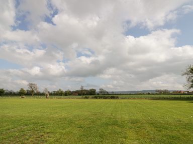 An open green field with trees and distant houses under a cloudy sky at Cotswold View 1 in Honeybourne
