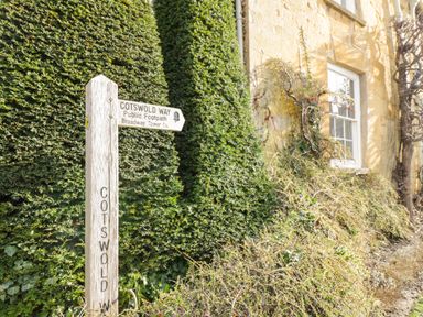 A wooden signpost for Cotswold Way public footpath near a hedge and a stone house at Cotswold View 1 in Honeybourne