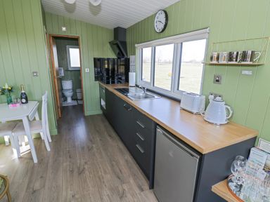 A kitchen with green walls black cabinets a wooden countertop and a dining table with chairs at Cotswold View 1 Honeybourne