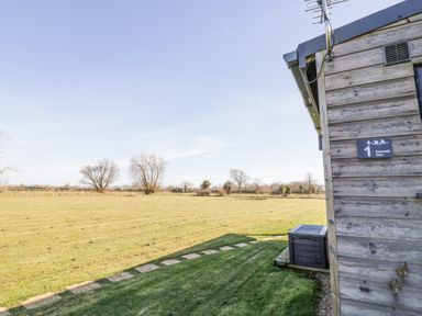 A grassy field with trees and a wooden building with a sign reading Cotswold View 1 in Honeybourne