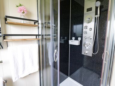A shower area with black speckled walls a silver shower panel and a towel rack with a white towel and pink flower at Cotswold View 2 in Honeybourne
