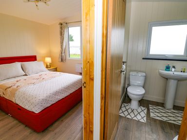 A bedroom with a bed and a nightstand with a lamp next to a bathroom with a toilet and sink at Cotswold View 2 in Honeybourne