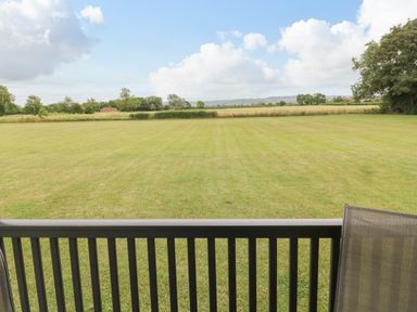 A large grass field viewed from behind a railing with trees and hedges in the distance at Cotswold View 2 in Honeybourne
