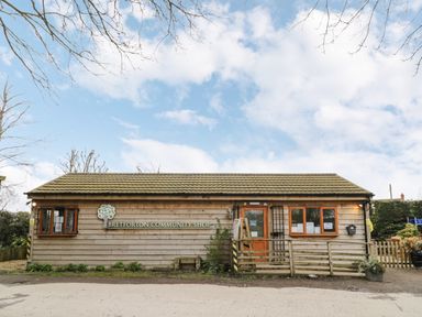 The exterior of Bretforton Community Shop a single story wooden building with windows a door and a small fenced area