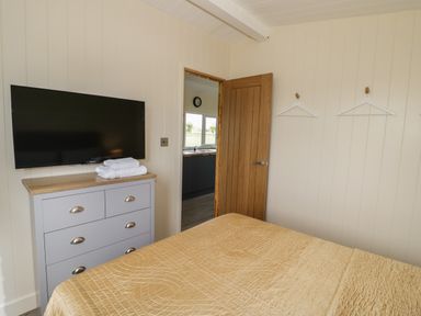 A bedroom with a bed covered in a yellow bedspread a chest of drawers with towels on it and a wall-mounted TV at Cotswold View 3 Bretforton near Evesham