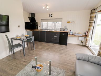 A kitchen and dining area with black cabinets a glass table set for two and a gray sofa at Cotswold View 3 Bretforton near Evesham