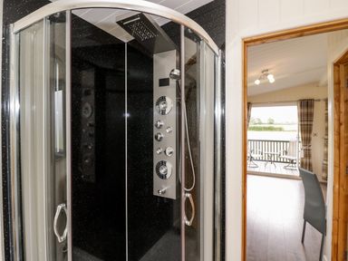 A bathroom with a shower enclosure next to a doorway leading to a room with chairs and a balcony at Cotswold View 3 Bretforton near Evesham