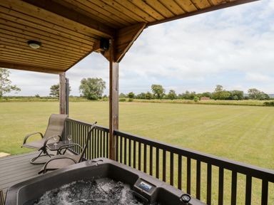A covered outdoor deck with a hot tub and two chairs overlooking a large grassy field at Cotswold View 3 in Bretforton near Evesham