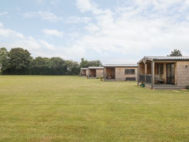 Four wooden cabins on a large grassy field with trees in the background at Cotswold View 3 Bretforton near Evesham