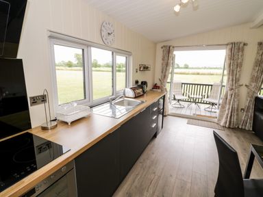A kitchen with wooden countertops and black cabinets overlooking a garden with open doors leading to a deck with two chairs at Cotswold View 4 in Bretforton near Evesham
