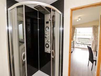 A bathroom with a black corner shower and a room visible through the doorway featuring a chair and an open patio door at Cotswold View 4 Bretforton near Evesham
