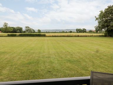 A large grassy field with trees and hills in the background at Cotswold View 4 in Bretforton near Evesham