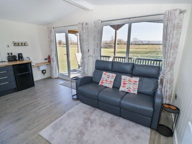 A living room with a gray sofa and sliding glass doors opening to a grassy field at Cotswold View 4 in Bretforton near Evesham