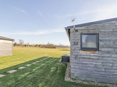 A wooden cabin with a small window and a grassy area with stepping stones at Cotswold View 4 in Bretforton near Evesham