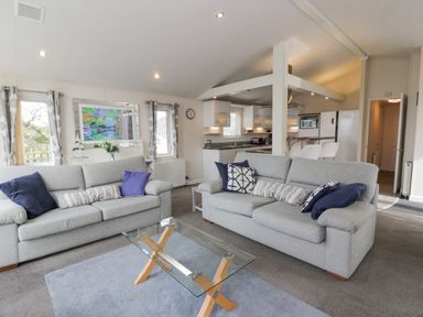 A living room with two gray sofas and a glass coffee table near a kitchen at Oyster Bay Lodge in Dalbeattie