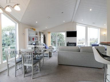 A living room with sofas and a dining table with chairs next to large windows at Oyster Bay Lodge in Dalbeattie