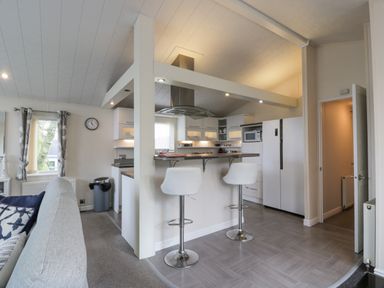 A kitchen with bar stools, refrigerator, microwave and a window next to a living area at Oyster Bay Lodge in Dalbeattie