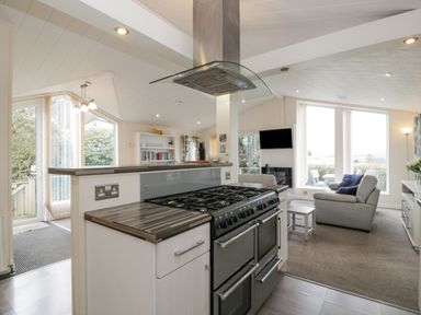 A kitchen with a stove and a hood vent next to a living room with sofas and a wall-mounted television at Oyster Bay Lodge in Dalbeattie