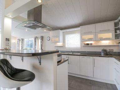 A kitchen with white cabinets a black and white bar stool a silver kettle and a toaster at Oyster Bay Lodge in Dalbeattie