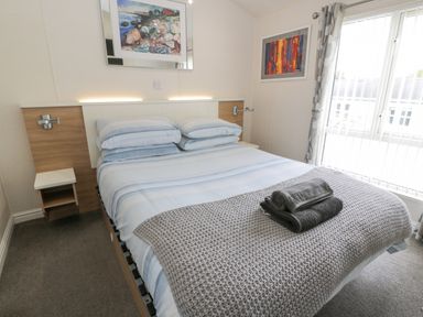 A bedroom with a bed with blue striped bedding and folded towels on top with artworks on the walls at Oyster Bay Lodge in Dalbeattie