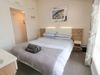 A bedroom with a double bed, bedside tables, wall art, and a door at Oyster Bay Lodge in Dalbeattie
