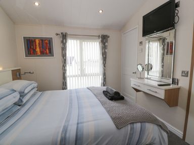 A bedroom with a bed made with striped bedding a wall-mounted television a mirror and a window with curtains at Oyster Bay Lodge in Dalbeattie