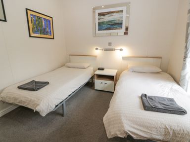 A bedroom with two single beds and a nightstand with a clock at Oyster Bay Lodge in Dalbeattie