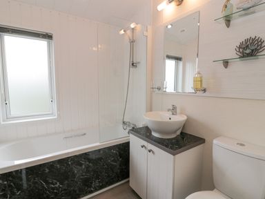 A bathroom with a bathtub shower combination a sink cabinet and a toilet at Oyster Bay Lodge in Dalbeattie