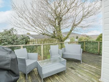 An outdoor wooden deck with gray wicker furniture and a barbecue grill at Oyster Bay Lodge in Dalbeattie