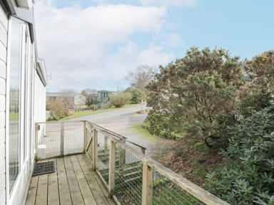 A wooden deck with railing outside a white building overlooking a road and bushes at Oyster Bay Lodge in Dalbeattie