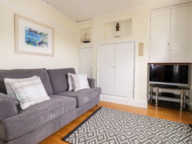 A living room with a gray sofa and patterned rug a TV on a stand and built in cupboards at Tresawle in Crantock