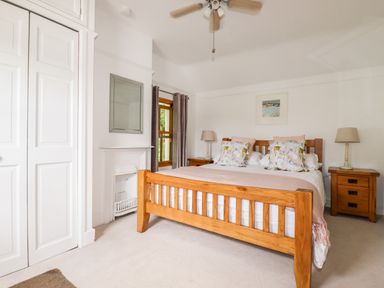 A bedroom with a wooden bed frame, two bedside tables with lamps, a window with curtains, and a white wardrobe at Tresawle in Crantock