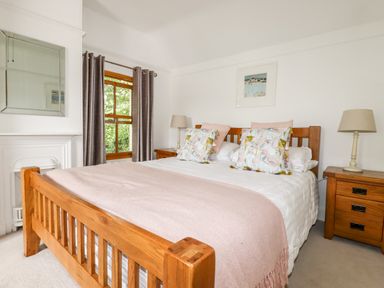 A bedroom with a wooden bed frame white bedding pink throw pillows and two wooden bedside tables with lamps at Tresawle Crantock