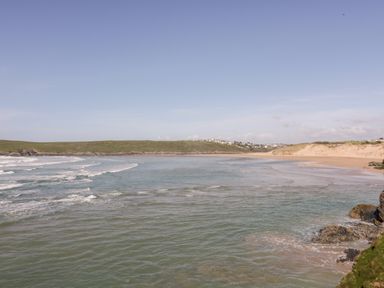 A beach with waves and rocks with houses on hills in the background at Tresawle in Crantock