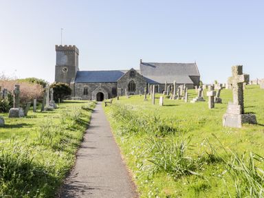 A church with a clock tower and gravestones on both sides of a path in a graveyard