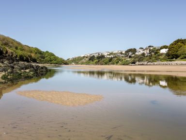 A river flowing through a valley with houses on the hillside and greenery on both sides at Tresawle in Crantock