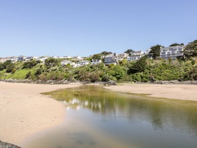 A sandy beach with a shallow water stream and houses on a hill covered with trees at Tresawle in Crantock