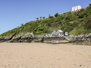 A sandy beach with a small dock and boathouse by a green hillside at Tresawle in Crantock