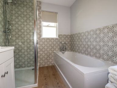 A bathroom with a bathtub and a shower enclosure with patterned tiled walls at Tresawle in Crantock