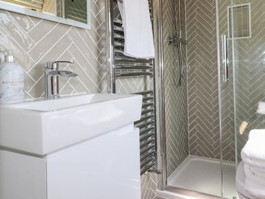 A bathroom with a white sink a chrome towel radiator towels and a glass shower enclosure at Tresawle in Crantock