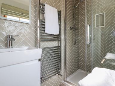 A bathroom with a sink a towel rail with a towel and a glass shower enclosure with a showerhead at Tresawle in Crantock