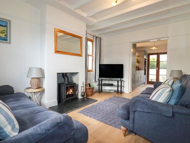 A living room with blue sofas a wood burning stove a TV and a doorway to a kitchen at Tresawle in Crantock