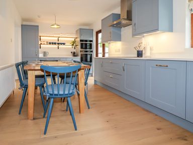 A kitchen with blue cabinets wooden dining table and blue chairs at Tresawle in Crantock